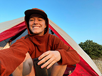 A woman smiling while sitting in the doorway of a camping tent.