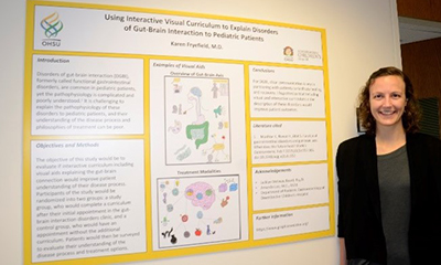 A woman smiling while standing next to her research poster.