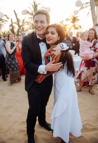 A man and a woman dressed in formal attire embracing on a beach.