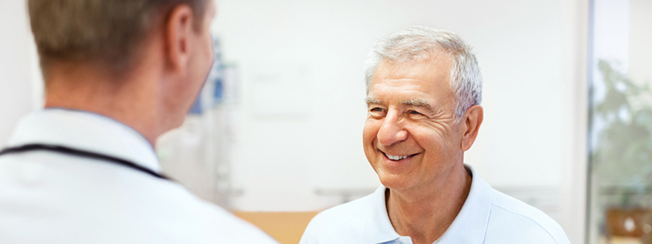 An older man smiling while speaking with another man, who is his doctor.