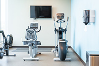 One side of the fitness room has a rowing machine, seated stationary bike, elliptical and TV. 