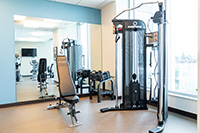 One side of the fitness room has a functional trainer with stack weights, free weights and an adjustable weight bench.