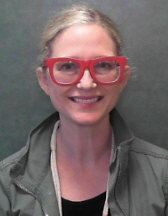 Carrie Milligan wearing red glasses and a green jacket