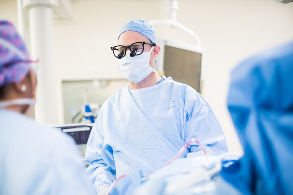 Dr. Daniel Dugi in surgical scrubs.