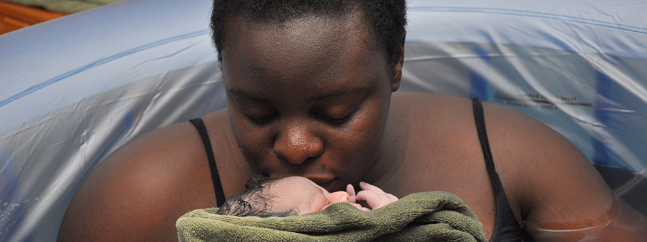 A woman kisses her newborn baby while relaxing in a birthing tub.