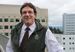 Smiling man, standing outside at OHSU, wearing a green vest, glasses and a tie