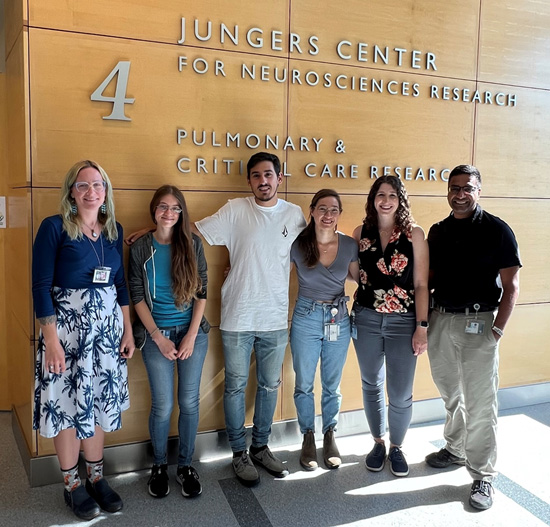 Unni lab members posed in front of the Jungers Center sign, smiling in the sunlight
