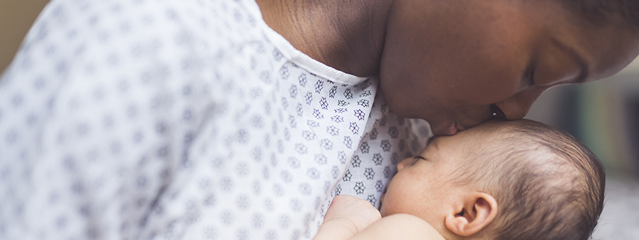 A new parent in a hospital gown snuggles and kisses her newborn.