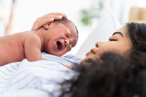Mother holds her close newborn in a warm, bright room.