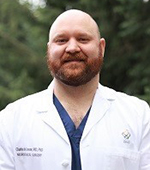 A man smiling outside wearing a doctor's white coat.