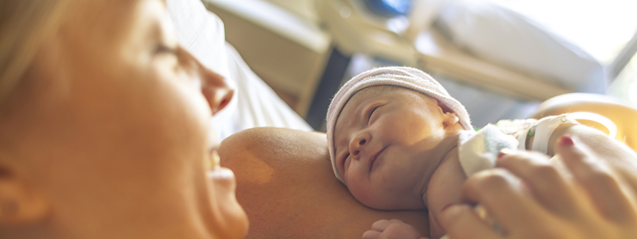 A new mom smiles at her newborn, resting skin-to-skin on her chest in a hospital room.