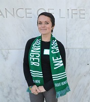 Nicky in front of a grey way with a green scarf
