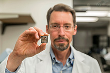 A researcher is holding a small chip that can analyze DNA.