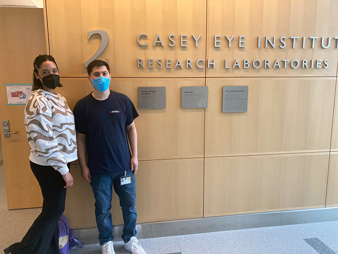 Two students pose standing in front of a research sign.