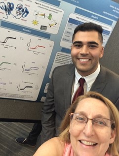 two smiling people standing in front of a research poster.