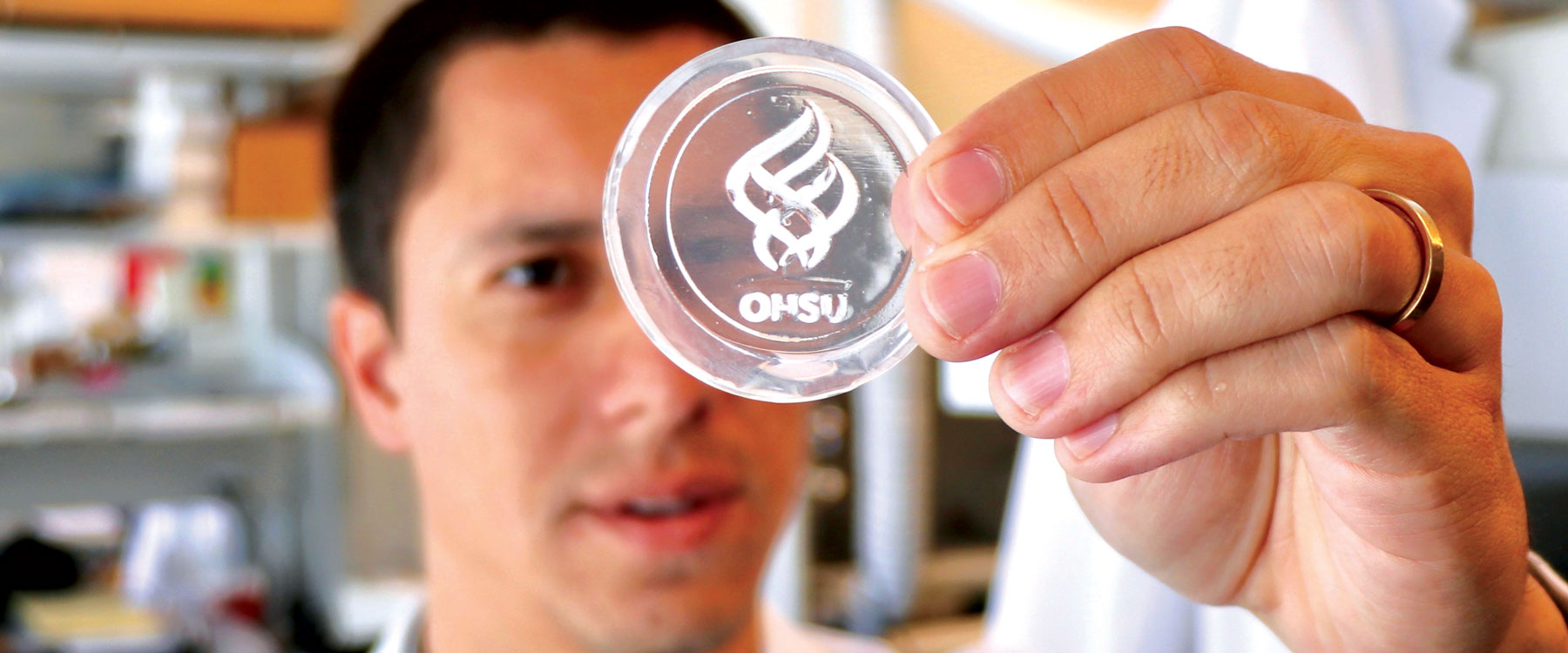 lab worker holding up a petri dish with OHSU logo