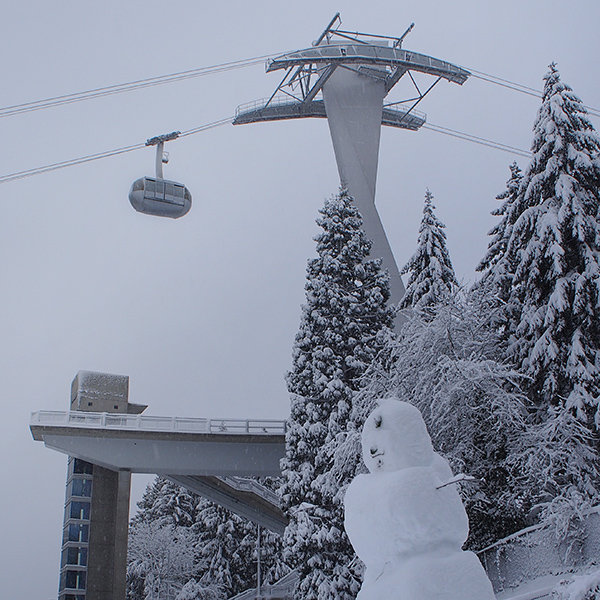 The Tram rises over a snowman and snow covered trees