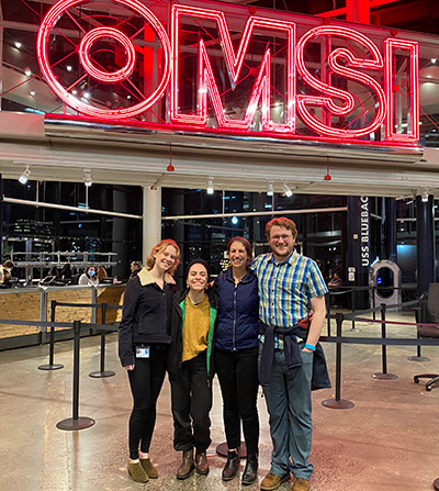 Four people in front of a sign.
