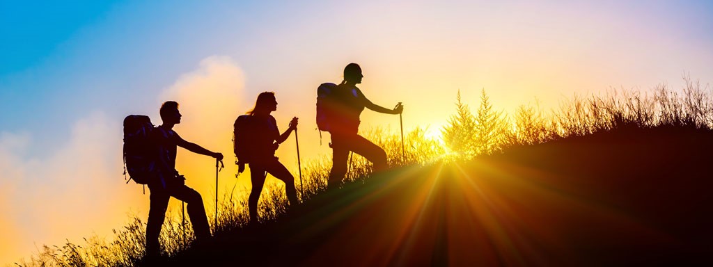 Three people are hiking up a mountain. They are silhouetted against the rising sun.