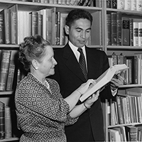 librarian helps student look at book in front of bookshelves