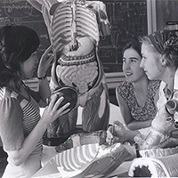 three nursing students talk in front of an anatomical model