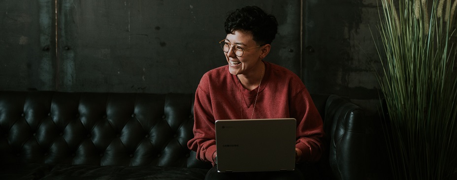 Picture of a laughing woman sitting on a black couch with a laptop