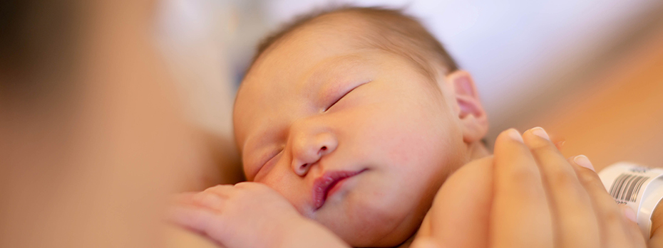 A newborn baby sleeps against an adult’s chest.