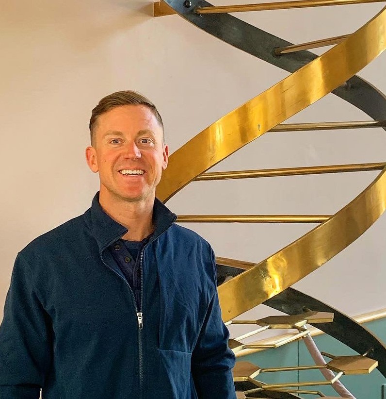Profile picture of SOD Researcher, Jonathon Baker, PhD, in front of a brass double helix sculpture.