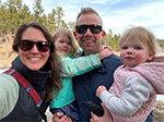 A man holding two female toddlers next to a woman outside on a sunny day.