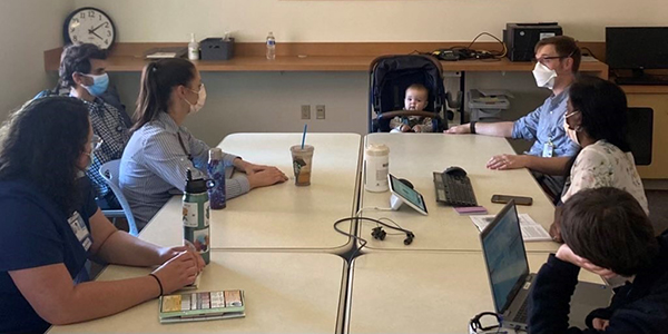 A photo of a group of residents sitting around a conference table, with a baby in a stroller at the head of the table.
