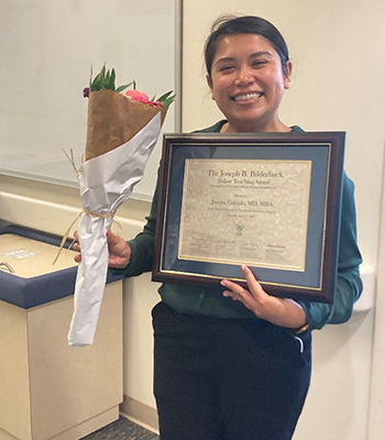 A photo of a woman holding a framed diploma and a bouquet of flowers.