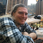 A man smiling outside in front of tall buildings.