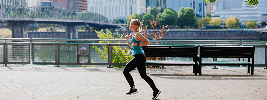 A woman runs along the Willamette River in Portland on a sunny day.