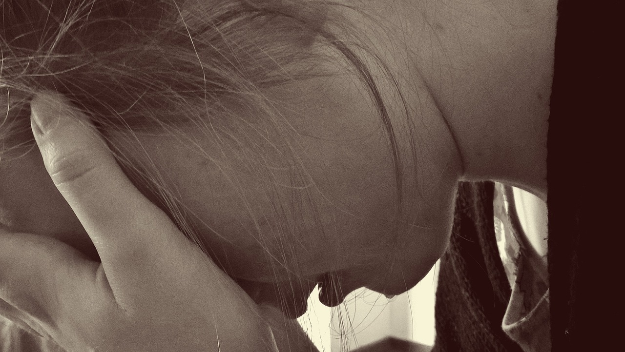A close up of young adult's face cradled in their hands, viewed from the side. The person has light skin and is crying.