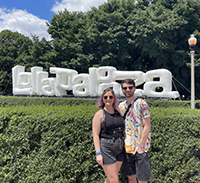 A man and a woman smiling outside in front of a "Lollapalooza" sign.