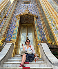 A woman smiling while sitting on the steps of an ornate doorway.