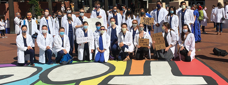 A group of 26 doctors, all wearing white coats and PPE masks, supporting "Black Lives Matter" in Pioneer Courthouse Square in downtown Portland, Oregon.