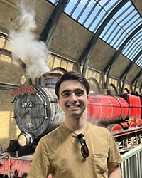 A man smiling in front of the Hogwarts Express at the Wizarding World of Harry Potter.