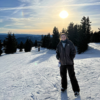 A woman standing and smiling on a snowy mountain on a sunny day.