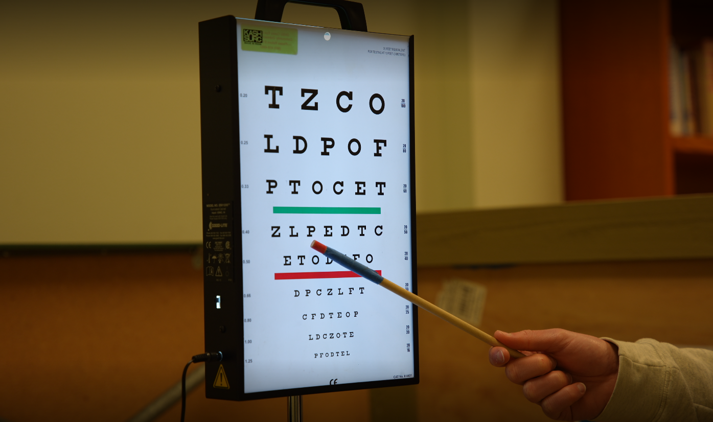 A hand holding a long pointer points to letters on an eye chart.
