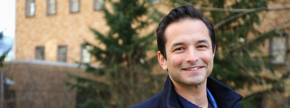 A doctor stands outside a medical building. His smile radiates warmth and reassurance.