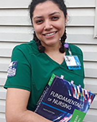 Nursing student Andrea Ruiz smiles at the camera while holding school books.