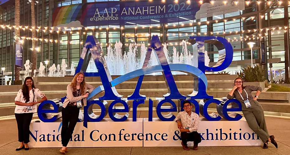 Three women and a man posing in front of a large sign that reads "AAP Experience National Conference and Exhibition."