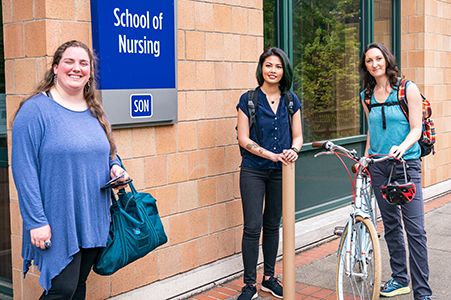 Three nursing students smile at the camera outside the Portland School of Nursing building.