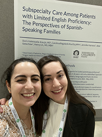 Two women smiling while posing in front of a research poster.