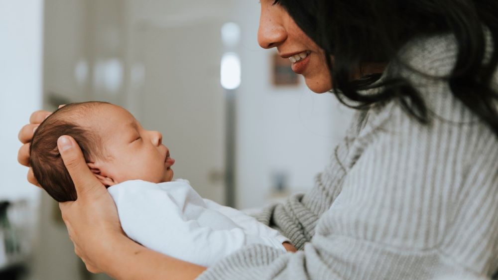A mother looks at her newborn face-to-face with a gentle smile.