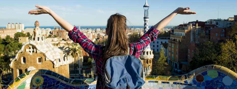 A student with long hair faces away from the camera while spreading their arms wide overlooking the city of Barcelona
