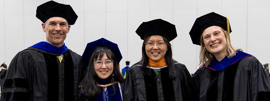 Four members of the biomedical engineering faculty pose side-by-side at graduation and smile. 