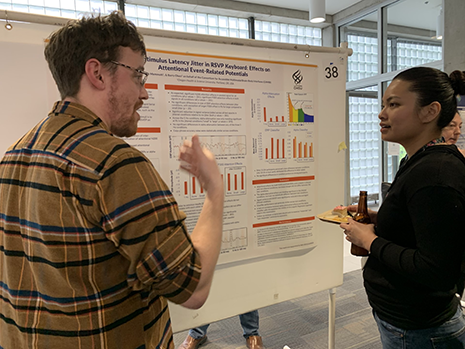 A man and woman having a conversation while standing in front of a research poster.