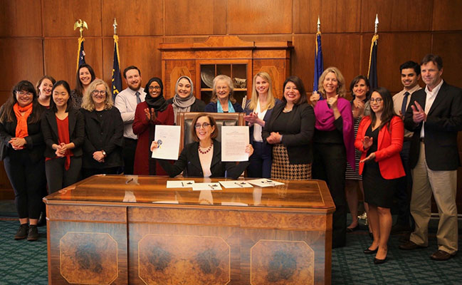 Oregon Govenor Kate Brown holds up two signed bills while surrounded by members of the public who contributed to the bill change.